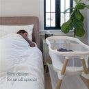 Baby in HALO BassiNest Essential Sleeper beside a sleeping woman, showcasing its slim design for small spaces.