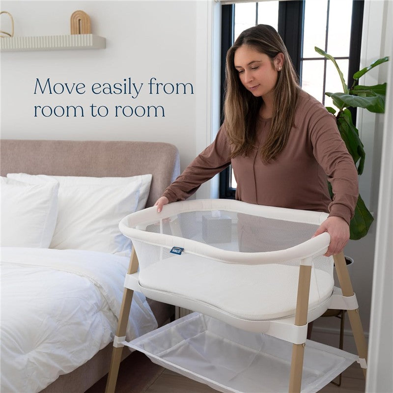 HALO BassiNest Essential Sleeper in white, being handled by a woman in a cozy bedroom, promoting easy room-to-room movement.