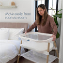 HALO BassiNest Essential Sleeper in white, being handled by a woman in a cozy bedroom, promoting easy room-to-room movement.