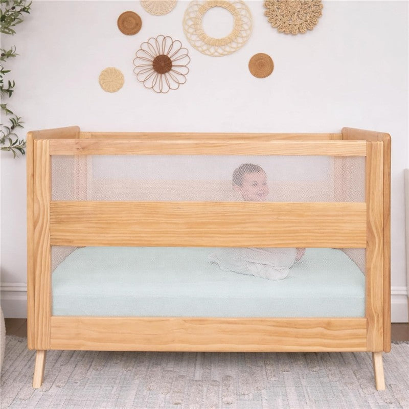 Fitted crib sheets in Calm Sage color are shown on a crib with a smiling infant visible through the mesh side.