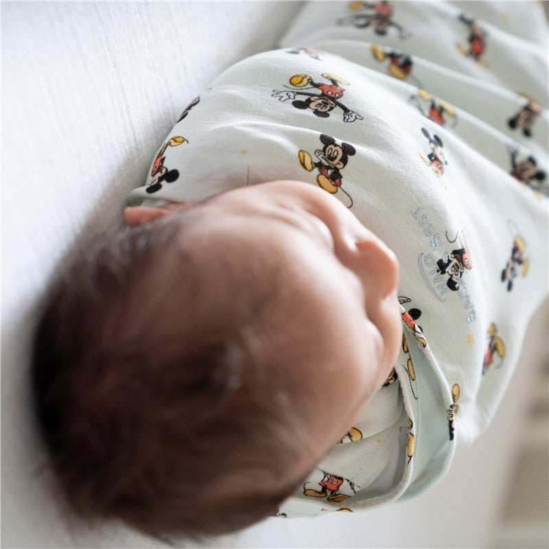 HALO SleepSack Swaddle in 100% cotton features a Mickey Mouse design, gently wrapping a sleeping baby.