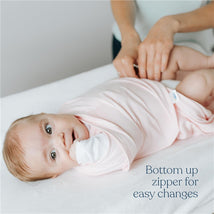 Baby wearing a pink HALO SleepSack Swaddle with a bottom-up zipper for easy changes, being held by a caregiver.
