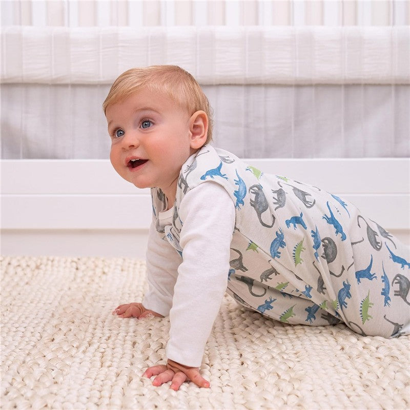 Baby crawling on a textured rug, wearing a HALO SleepSack blanket in a watercolor dinosaur pattern.