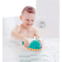 A child in a bubble-filled bath joyfully plays with the Hape Bubble Blowing Whale, a teal whale toy with orange stripes.