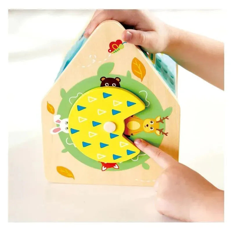 Colorful wooden shape sorter in the form of a house, with a hand guiding a triangular shape into the correct slot.