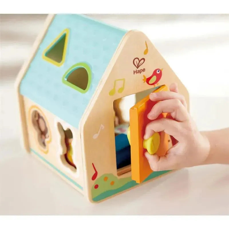 Hape Critter House Shape Sorter, featuring colorful shapes and a hand inserting a piece into the house.