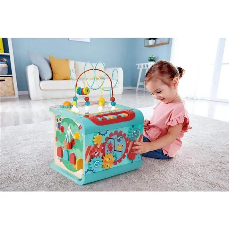 A smiling child interacts with the Hape Explore and Learn Magic Cube Montessori toy, featuring colorful beads, gears, and shapes.