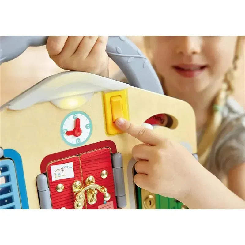 Child pressing a yellow button on the Hape Game Board Lock and Key, featuring various colored doors and a clock.