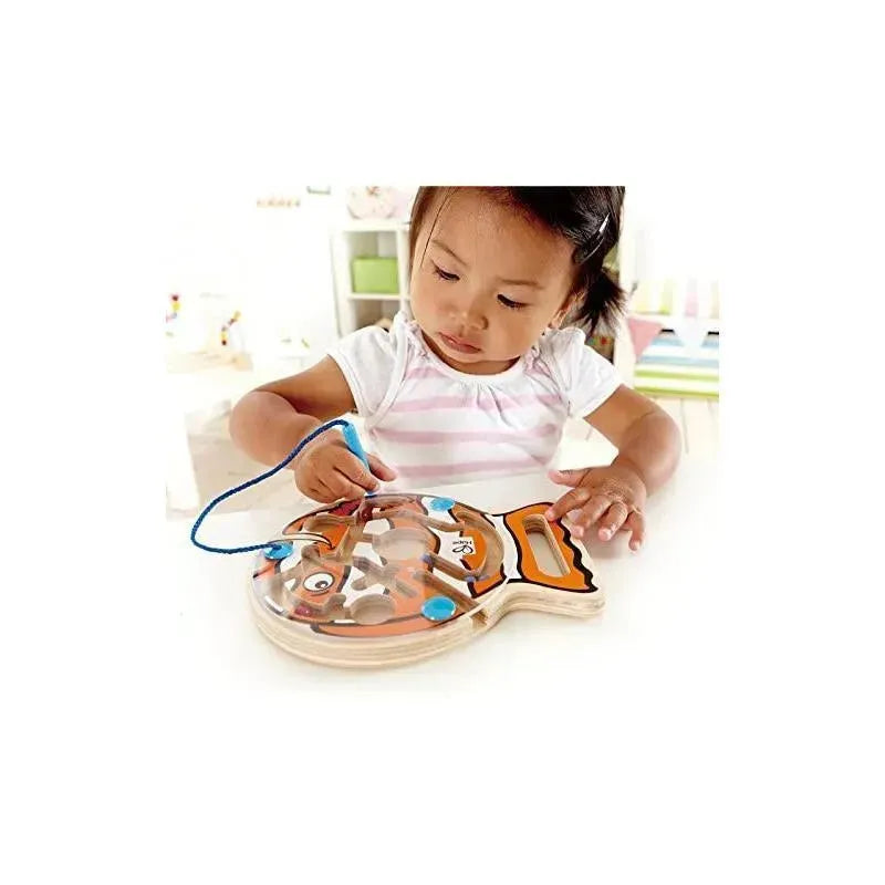 Toddler engaging with the Hape Go-Fish-Go magnetic maze puzzle, using a blue lacing tool to move beads.