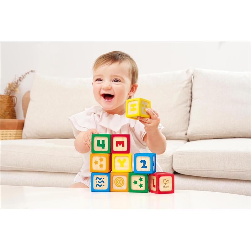 A happy baby playing with colorful Hape Grip-N-Stack silicone and wood blocks, stacking them on a table.