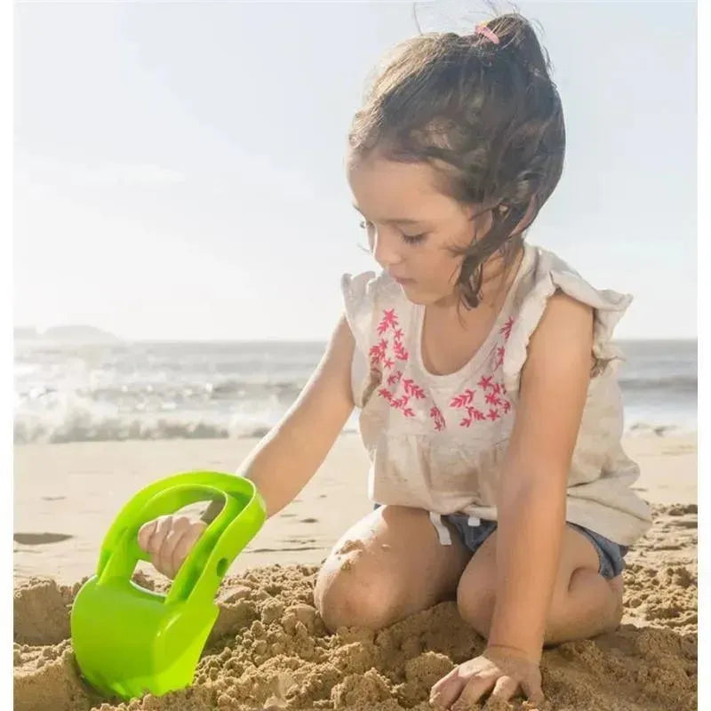 Child playing in sand with a green Hape hand digger toy at the beach, enjoying a sunny day.