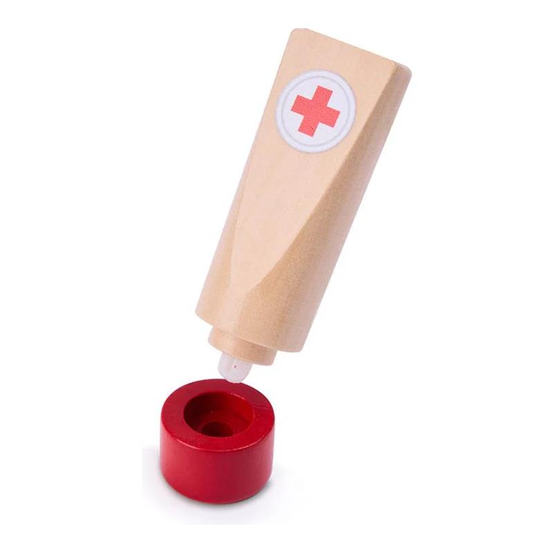 Wooden toy medical set piece resembling a tube of cream with a red cross symbol, tilted above a red circular base.