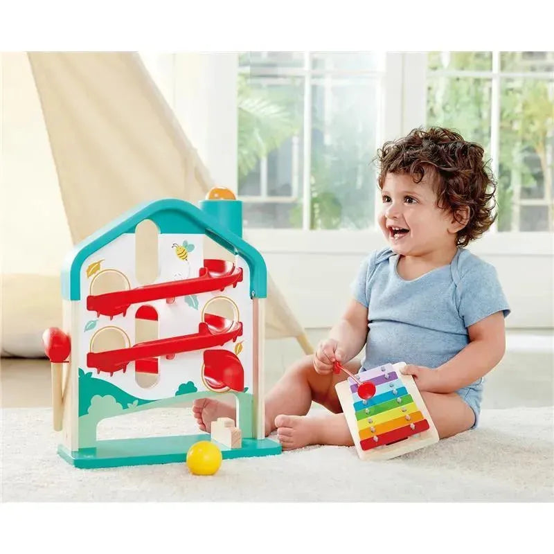 Toddler playing with Hape Melody Mansion Ball Run, featuring a colorful ramp and xylophone, smiling happily in a bright room.