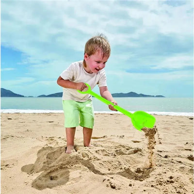 A child plays on the beach, joyfully using a bright green Hape Mighty Sand Shovel to dig in the sand.