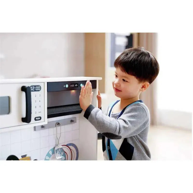 A young boy interacts with the modern Hape Smart Kitchen, using a digital microwave display.