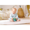 A baby in a light blue outfit plays with the Hape Music Turtle toy, featuring colorful musical elements, on a soft rug.