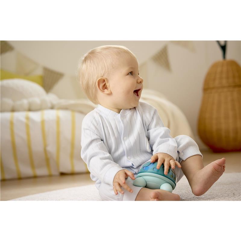 Happy baby in a white striped outfit sitting on the floor, playing with the Hape Music Turtle toy.