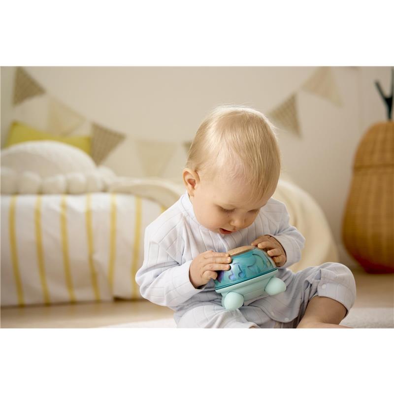 A baby in pajamas interacts with the Hape Music Turtle toy, focusing on its colorful musical features.