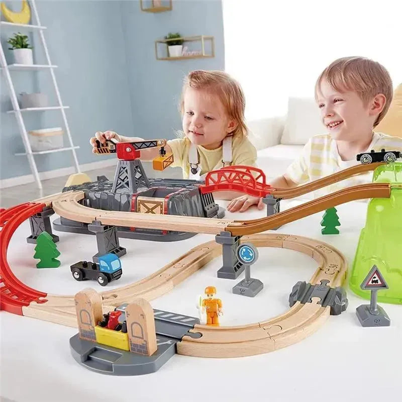 Children interact with the Hape Railway Bucket Builder Set, featuring wooden tracks, a crane, and vehicles on a playtable.