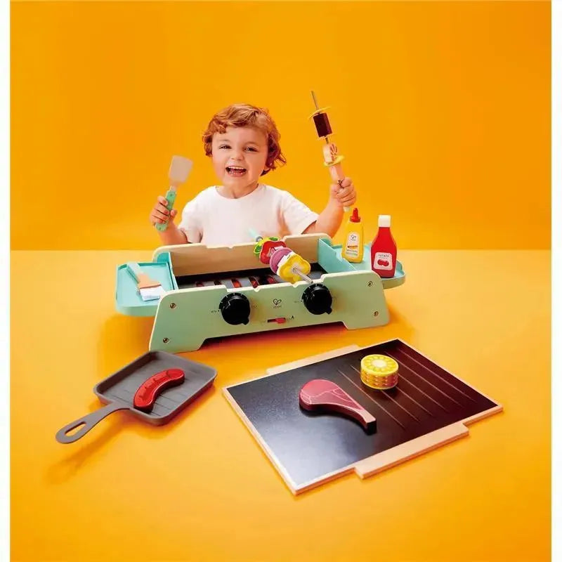 Child interacting with the Hape Sizzling Griddle & Grill BBQ toy, holding a spatula and a skewer with colorful food items.