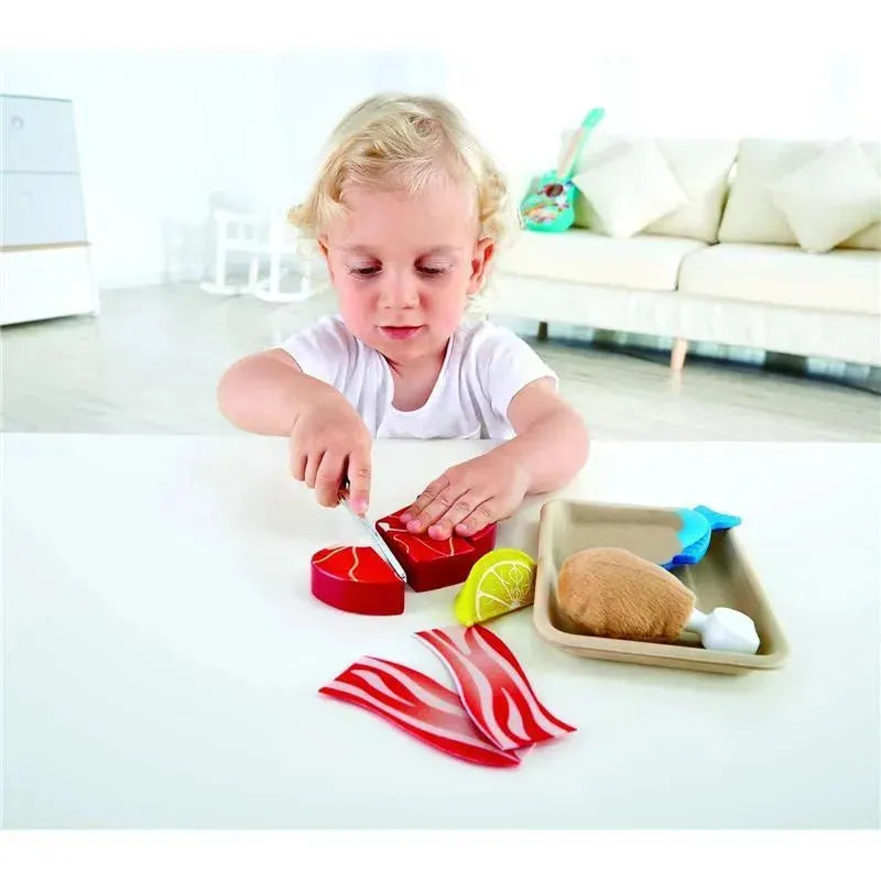 Child playing with Hape Tasty Proteins Set, using a toy knife to cut colorful, realistic-looking food items on a table.