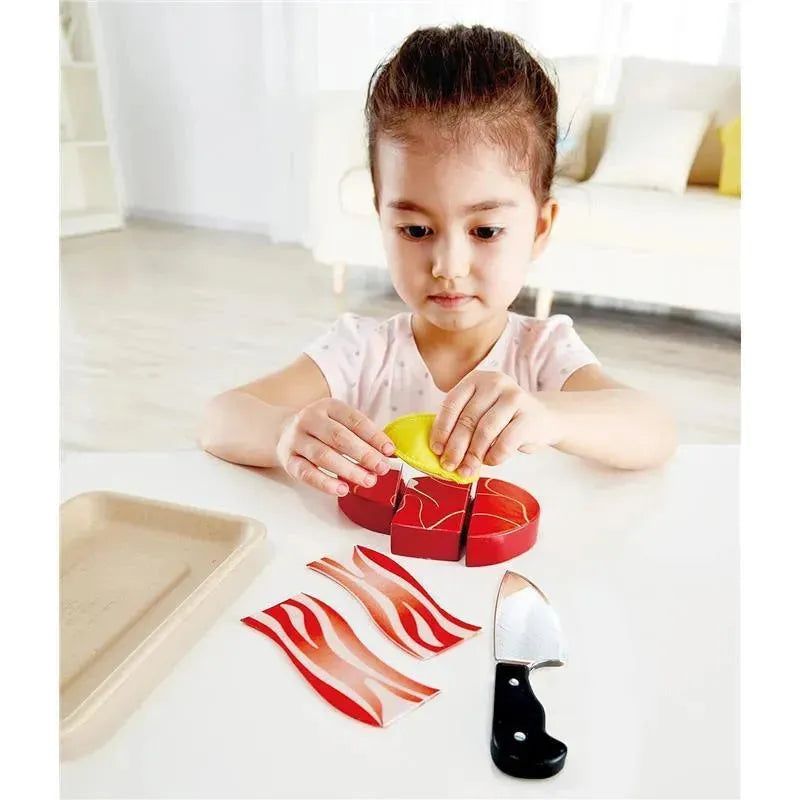 Child assembling a toy food set, featuring colorful food pieces like sliced meat and a knife on a table.