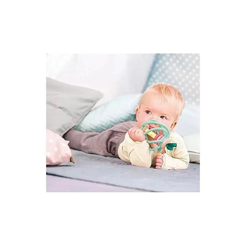 A baby lies on a soft surface, holding a colorful teeter totter toy, surrounded by pillows in a cozy setting.