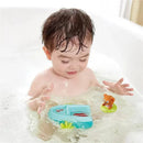 A child splashing in a bath plays with a blue pull-back boat toy and a small floating bear on a green ring.