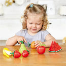 Child smiling while playing with wooden toy fruits, including bananas, strawberries, and a watermelon, using a play knife.