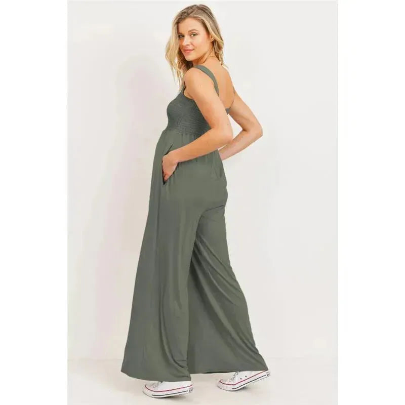 Olive green square neck smocked maternity jumpsuit with flared legs, model posing with hands in pockets.