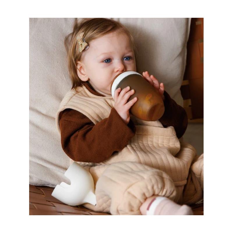 Toddler in a beige outfit drinking from a Heorshe ultra wide neck baby bottle, seated comfortably.