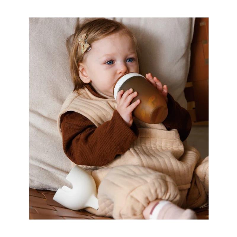 A child with light brown hair drinks from a Heorshe ultra wide neck black baby bottle while seated on a soft surface.