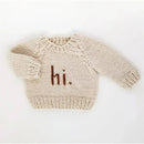 Cream-colored knit crew neck sweater for babies and toddlers with “hi.” embroidered in brown on the front.