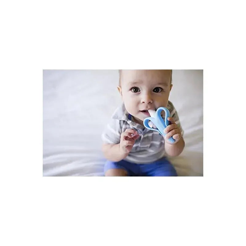 Infant holding a blue Baby Banana toothbrush, designed for early dental care, while sitting on a light-colored surface.