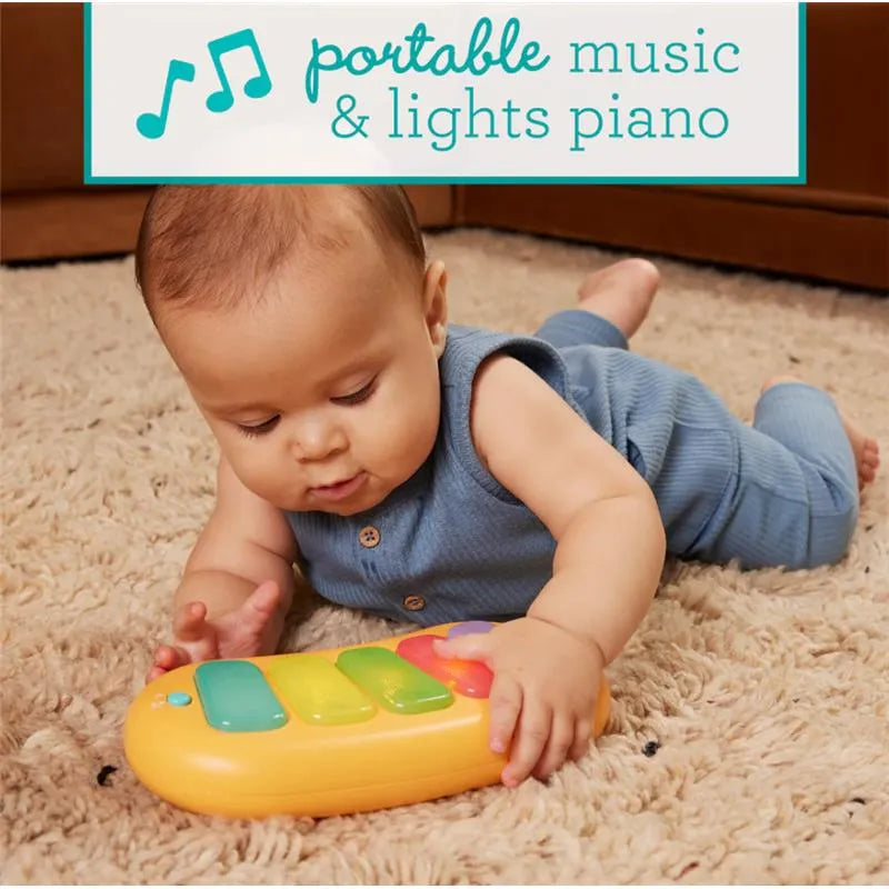 Infantino portable music and lights piano on the floor, with a baby lying on a carpet, reaching for the toy.