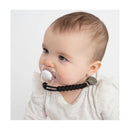 Baby with a clear pacifier attached to a black silicone holder, wearing a light-colored, ruffled shirt.