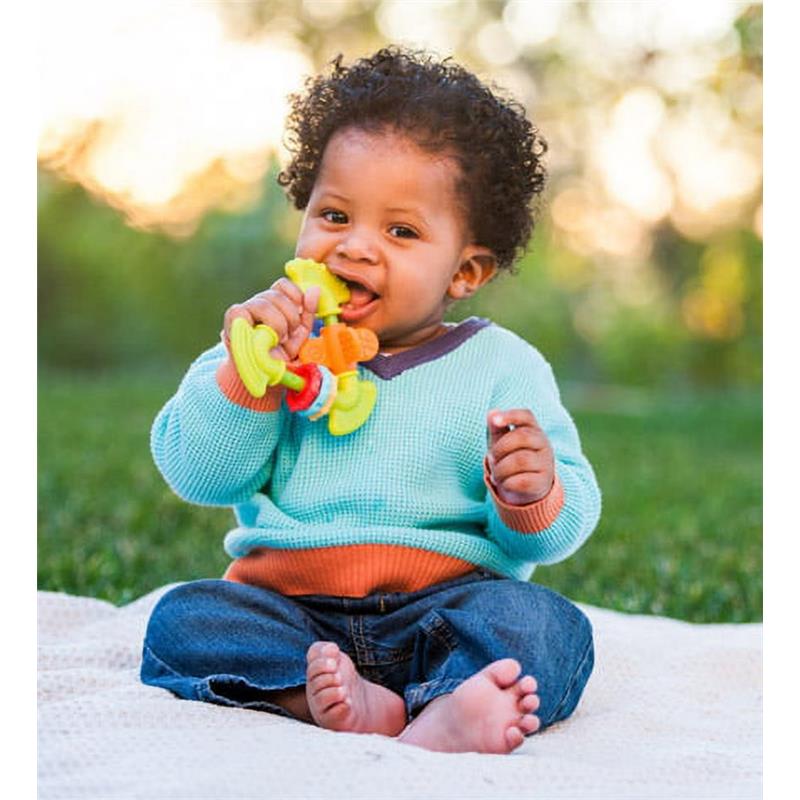 Infantino Chewy Activity Teether held by a smiling toddler sitting on a blanket in a grassy area, enjoying the colorful teether.