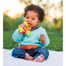 Infantino Chewy Activity Teether held by a smiling toddler sitting on a blanket in a grassy area, enjoying the colorful teether.