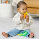 Infantino Farmers Market Teether Gift Set with a toddler sitting and chewing on an orange carrot teether, surrounded by more teething toys.