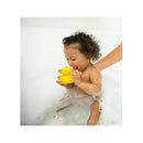 Baby with curly hair playing in a bubble bath, holding a yellow rubber duck, with a hand gently supporting them.
