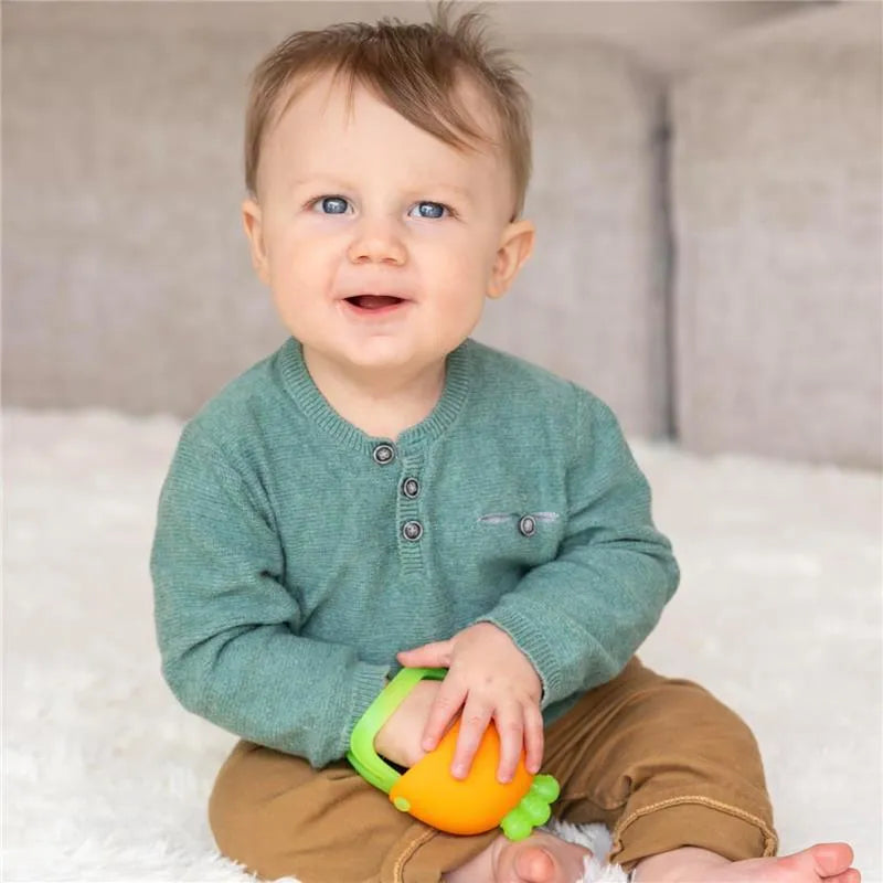 Smiling baby sitting on a soft surface, holding an orange carrot-shaped teething mitt.