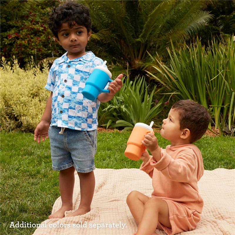 Two children in a garden hold colorful soft silicone tumblers. One child has a blue tumbler, the other an orange one.
