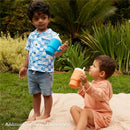 Two young children outdoors, one holding a blue Infantino My 1St Tumbler and the other holding an orange tumbler, both smiling.