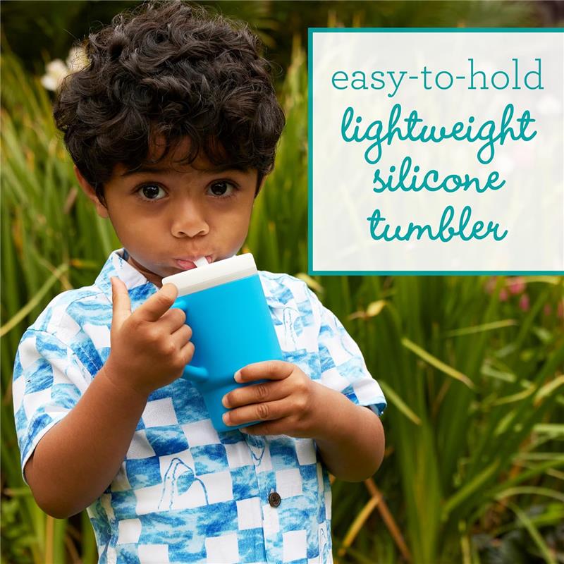 Child holding a blue silicone tumbler with a straw, wearing a patterned shirt, surrounded by greenery.