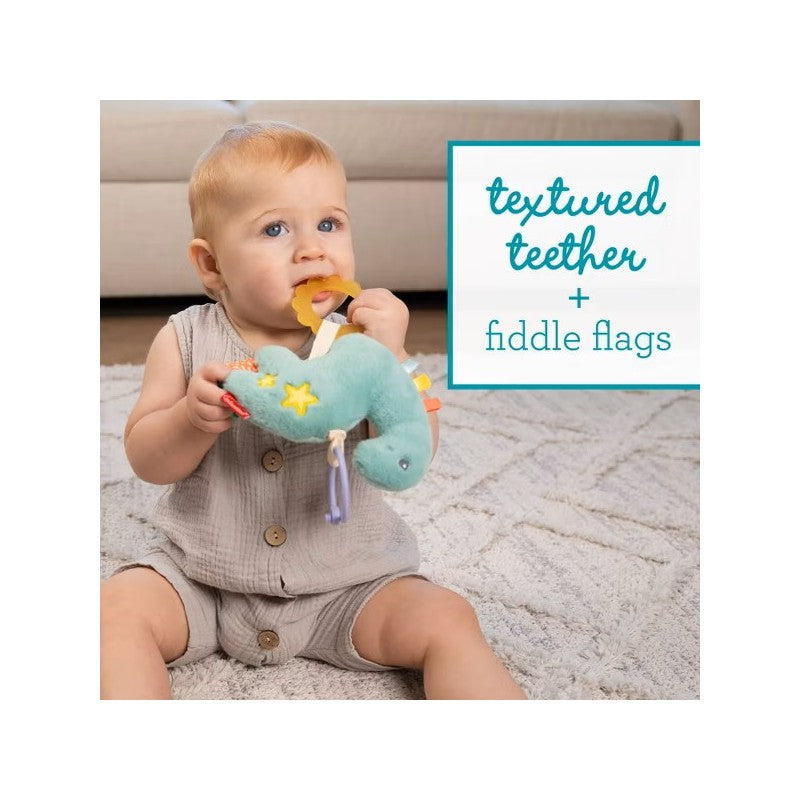 A baby sits on a rug, holding an Infantino Pull & Shake Jittery Pal Dino toy with textured teethers and fiddle flags.