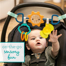 Infantino Sensory Travel Bar attached to a stroller, featuring colorful toys; a baby reaches out in curiosity.