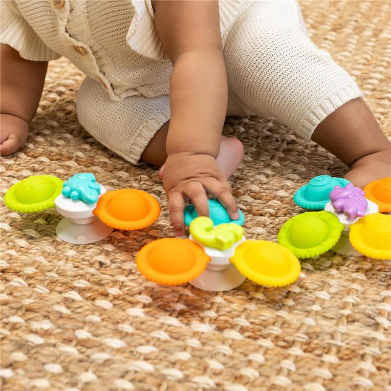 Colorful silicone bath spinners by Infantino, being played with by a child on a textured mat.