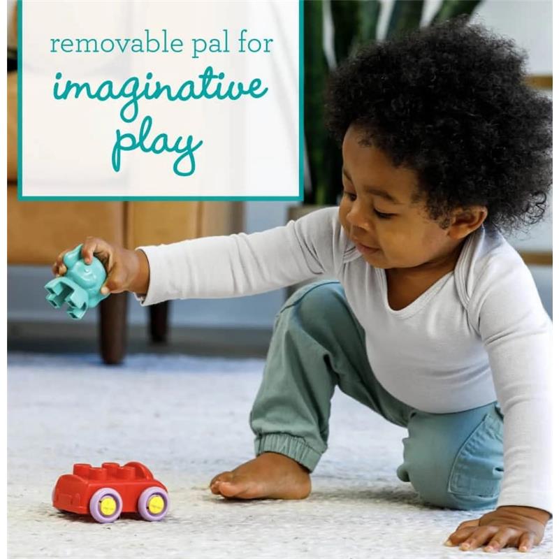 Child playing on a soft surface, holding a teal toy figure next to a red toy car with purple wheels.
