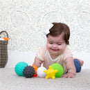 Multicolor Infantino Textured Multi Ball Set arranged around a smiling baby girl, who is playing on a soft surface.