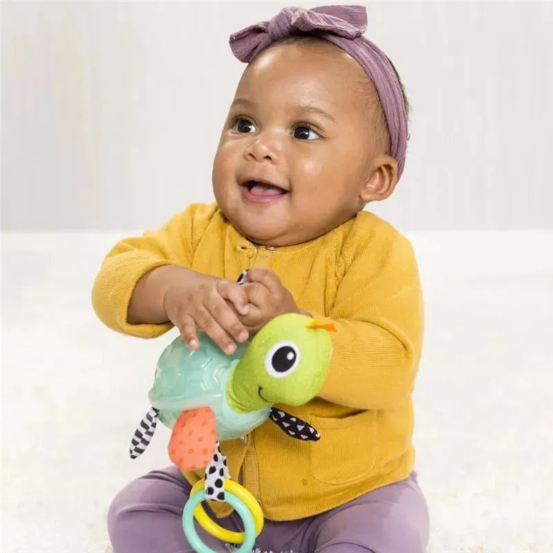Smiling baby wearing a yellow sweater holds the Infantino Textured Sensory Pal Turtle toy, featuring colorful textures and rings.